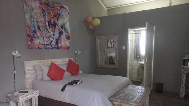 A bedroom with a bed, a small bedside table, a bench, a mirror, and a wall painting.