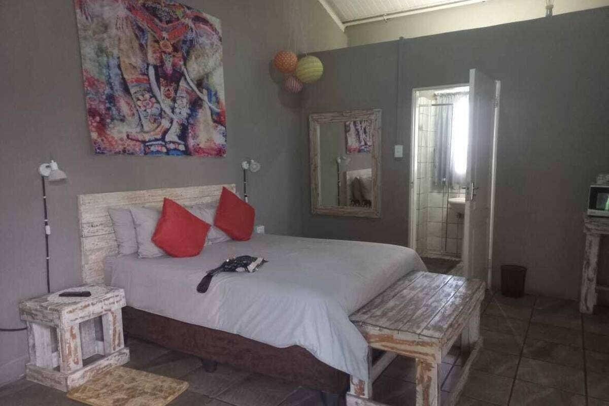 A bedroom with a bed, a small bedside table, a bench, a mirror, and a wall painting.