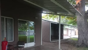 A covered outdoor area with a fire extinguisher, a chair, and a building with a metal roof.