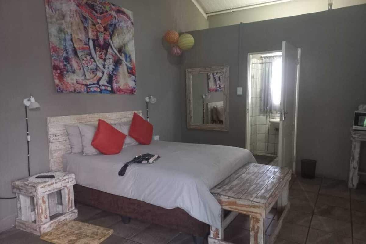 A bedroom with a bed, a bedside table, a nightstand, a mirror, and a wall with a colorful painting.