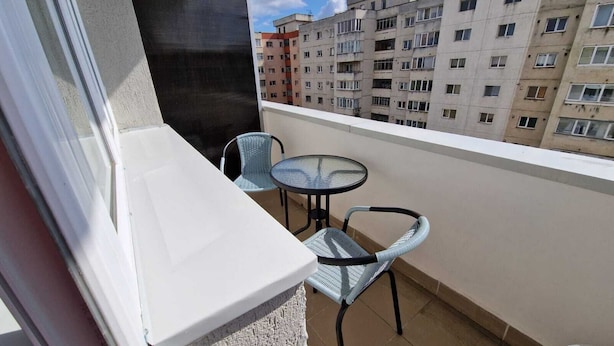 Ein Balkon mit einem kleinen Tisch und zwei Stühlen, der auf ein Wohngebäude blickt.