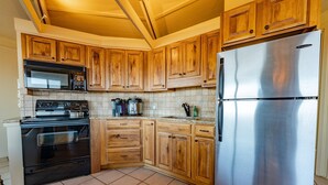 Eine Küche mit Holzschränken, einem Edelstahlkühlschrank, einer Mikrowelle, einem Backofen und einer Kaffeemaschine.