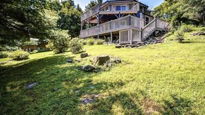 Ein mehrstöckiges Holzhaus mit einer Terrasse, umgeben von einem grünen Rasen und Bäumen.