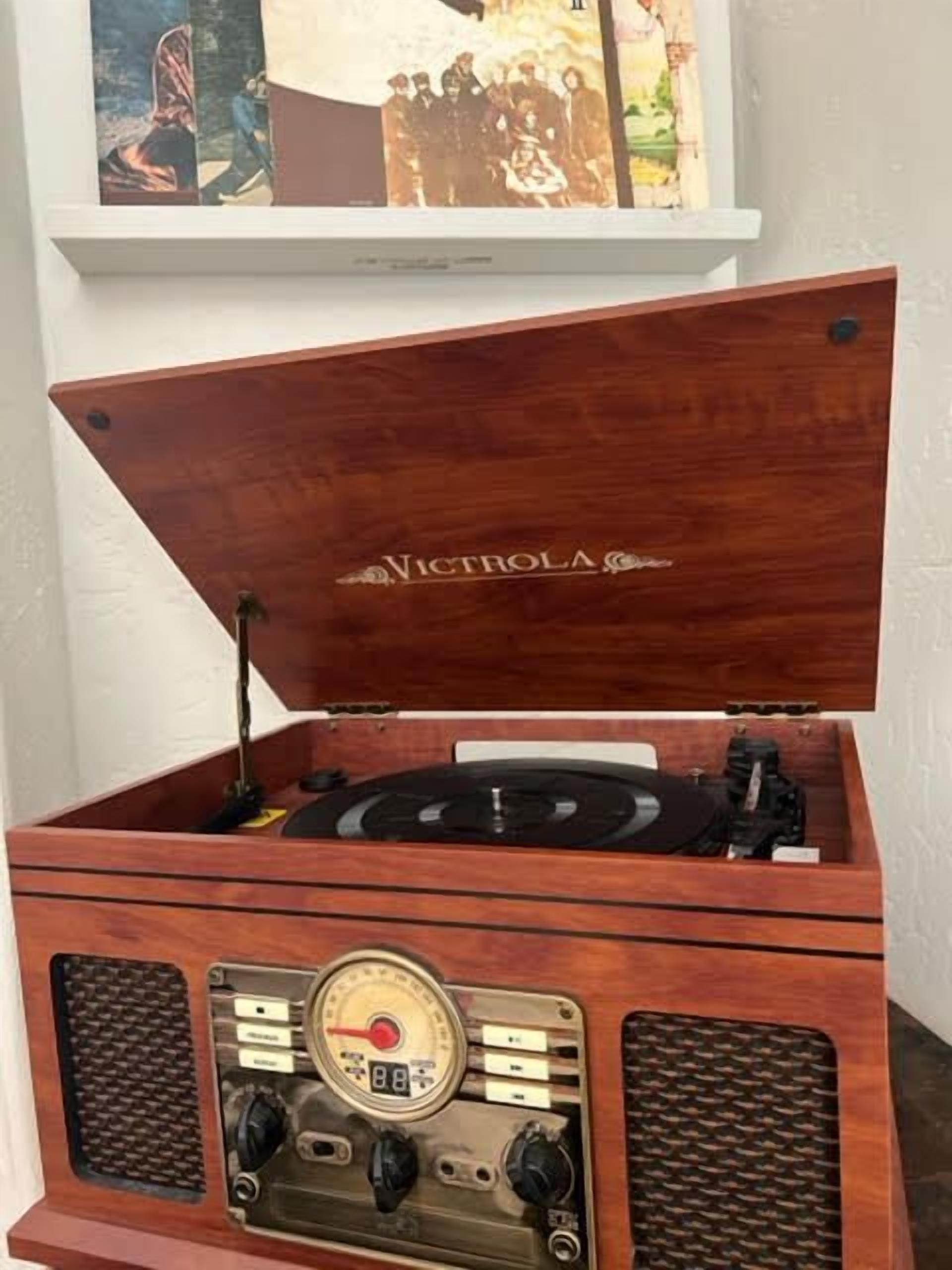 A wooden record player with a brand name "VICTROLA" on the lid, placed on a white shelf.