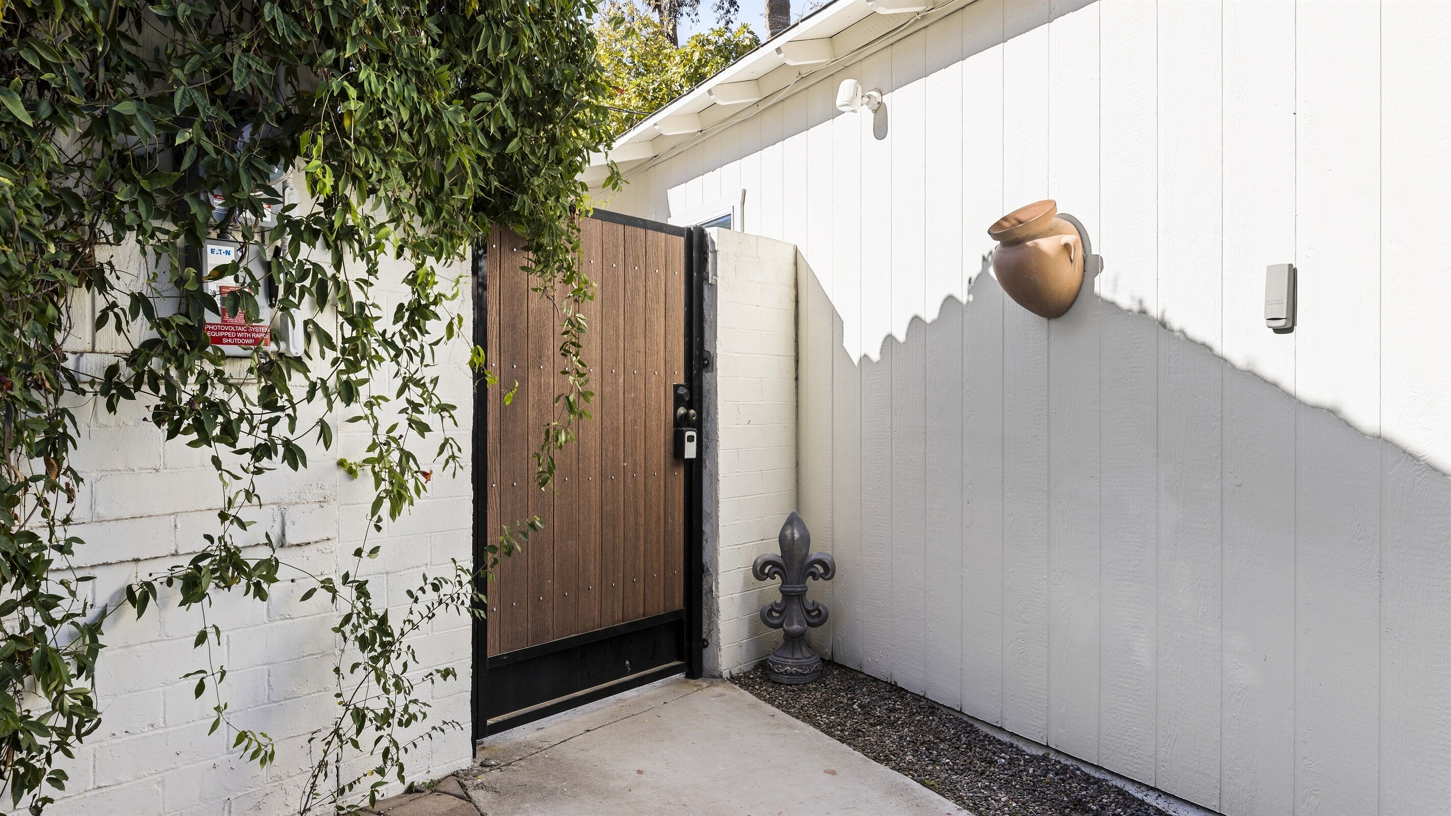 A gated entrance with a wooden door, a white wall, and a decorative pot.