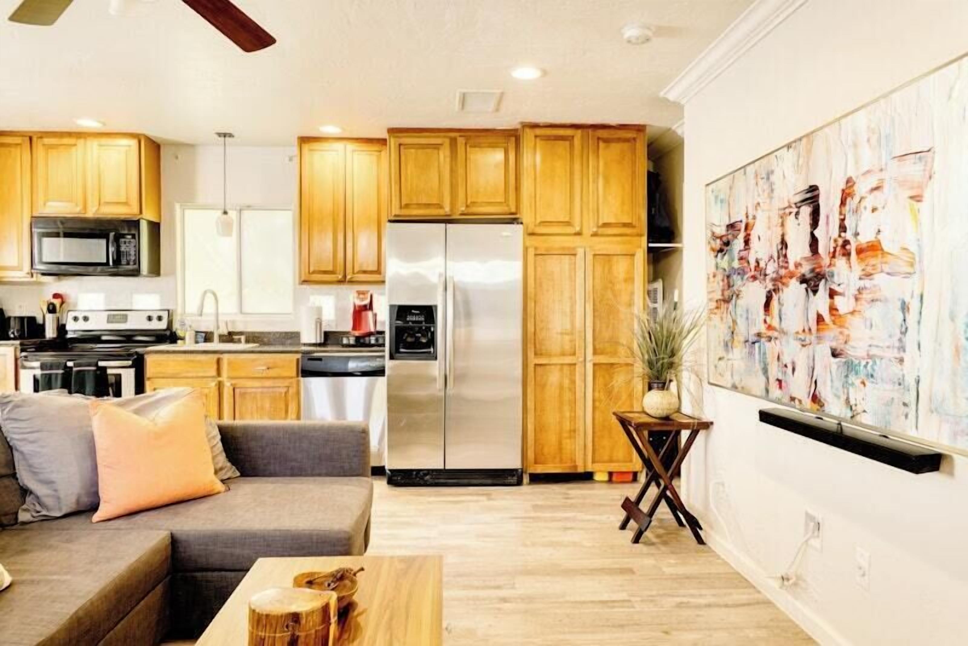 A modern kitchen with wooden cabinets, stainless steel appliances, and a dining area with a gray sofa and a small wooden table.