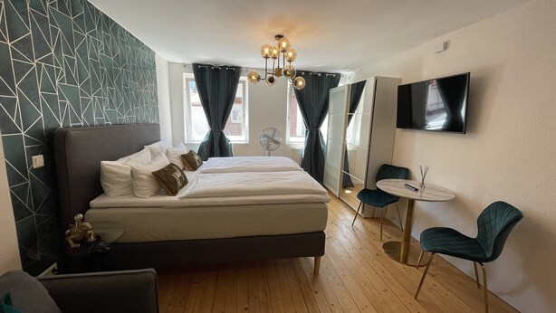 Quarto de hotel com uma cama grande, uma escrivaninha com cadeira, televisão e espelho.