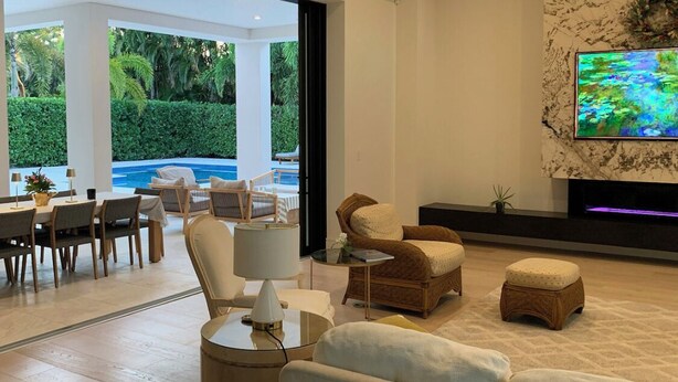Un salon moderne avec vue sur la piscine, doté de sièges confortables et d’un téléviseur à écran plat fixé sur un mur en marbre.