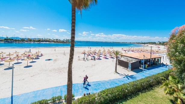Een strand met parasols, een redershut en een helderblauwe lucht.