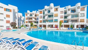 Een resort met een groot zwembad, omringd door ligbedden en een modern gebouw met balkons.