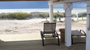 En træterrasse med en stol og et lille bord, med udsigt over en strand med bølger og en klar himmel.