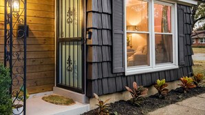 A house with a wooden exterior, a sliding glass door, and a window with shutters. - The Jungalow: 65" 4K TV, memory foam, kid-friendly (Louisville)