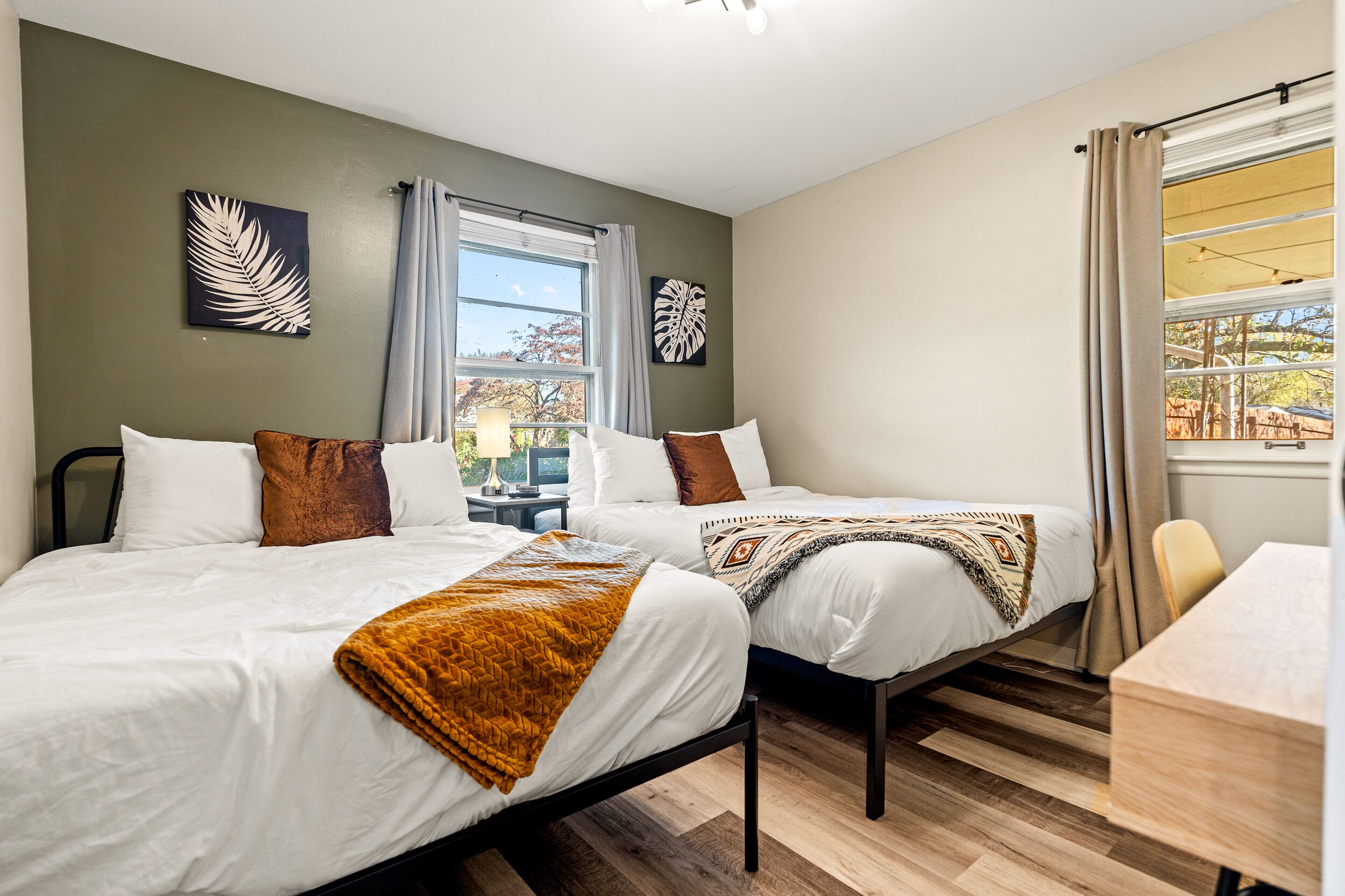 A bedroom with two beds, a window with curtains, and artwork on the walls.