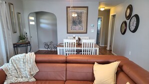 Ein braunes Ledersofa mit Überwurfdecke und zwei Kissen, ein Esstisch mit Stühlen und eine Wand mit vier Uhren.