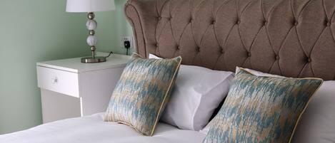 A neatly made bed with white linens and two decorative pillows, a bedside table with a lamp, and a wall socket.