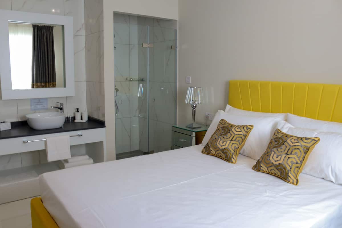 Une chambre d’hôtel avec un grand lit, une salle de bain équipée d’un lavabo et d’un miroir, et une douche à parois de verre.