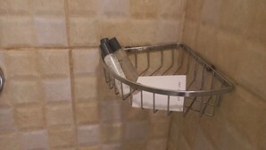 Cestino metallico con articoli da toilette e un cartoncino bianco, fissato a una parete piastrellata.