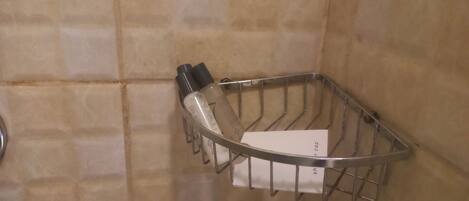 Un panier en métal contenant des articles de toilette et une carte blanche, fixés à un mur recouvert de carreaux.