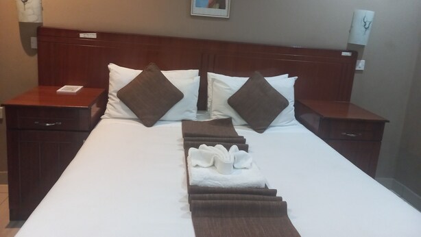 A hotel room with a large bed, two nightstands, a headboard, and a framed picture on the wall. - ShakeVille Guest House (Shakawe)