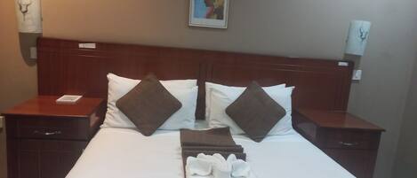 A hotel room with a large bed, two nightstands, a headboard, and a framed picture on the wall.