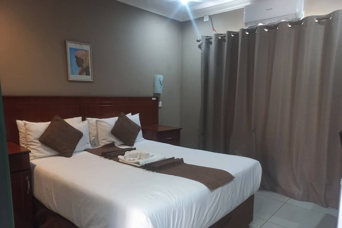 A hotel room with a neatly made bed, a nightstand, a wall-mounted lamp, and a window with curtains.