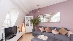 Ett modernt vardagsrum med en grå soffa, en platt-TV, ett vitt skåp och en stor spegel på väggen.