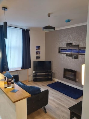 A modern living room with a sofa, a TV, and a wooden coffee table. - Apartment49Oban, very close to Town center. (Oban)