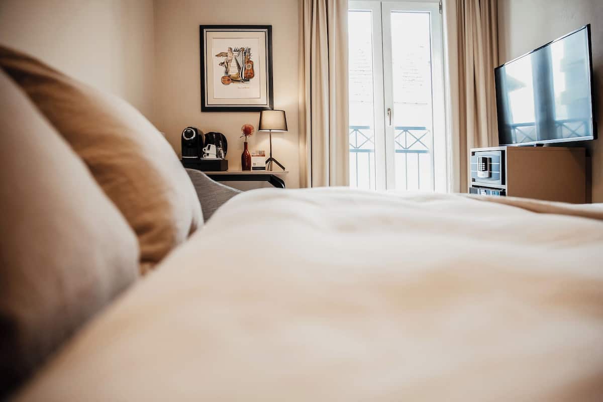 Camera d'albergo con un letto, una televisione, un quadro appeso al muro, un comodino con una lampada e vista su un balcone.