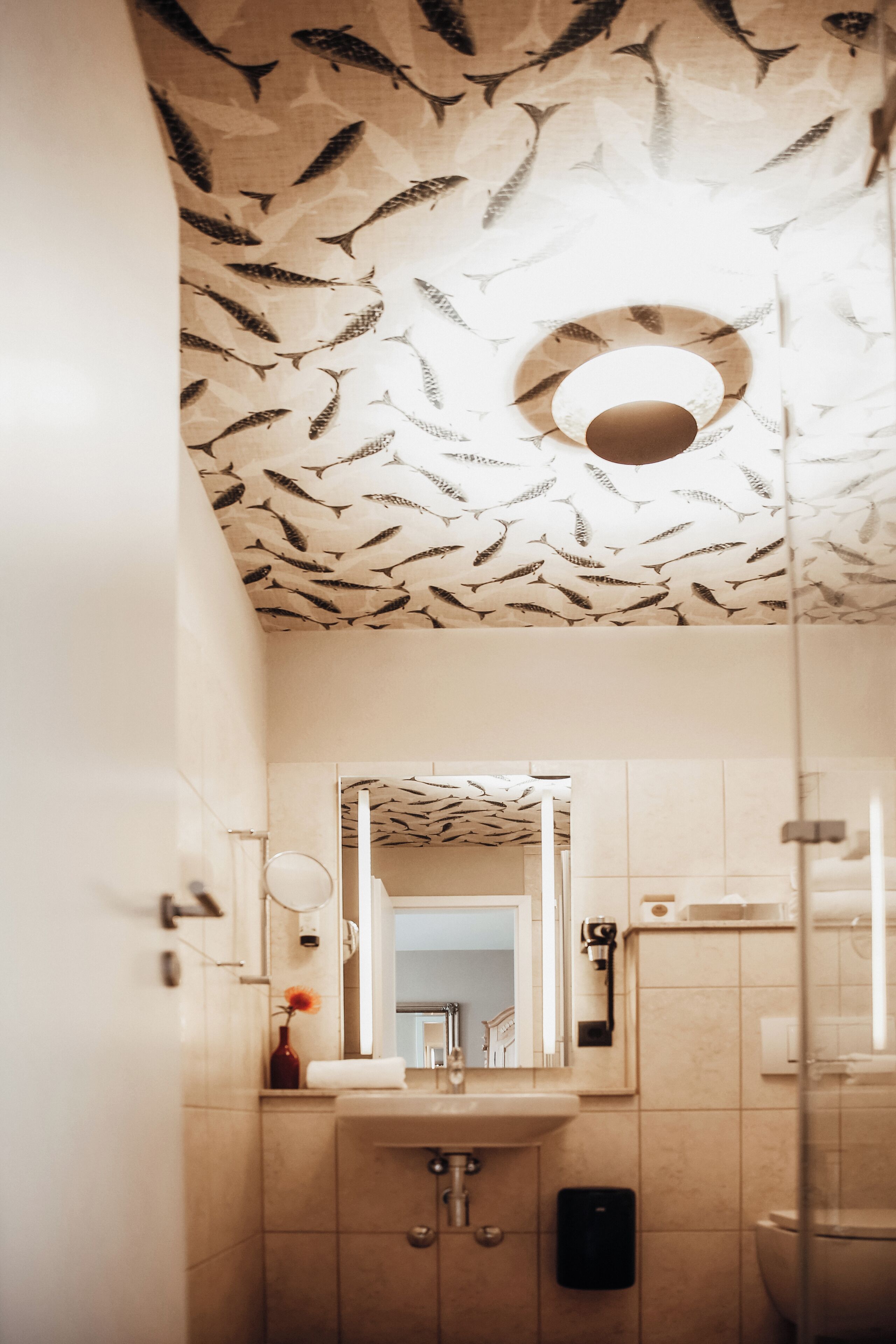 Ein Badezimmer mit Fischmuster an der Decke, einem Waschbecken, einem Spiegel und einer Toilette.