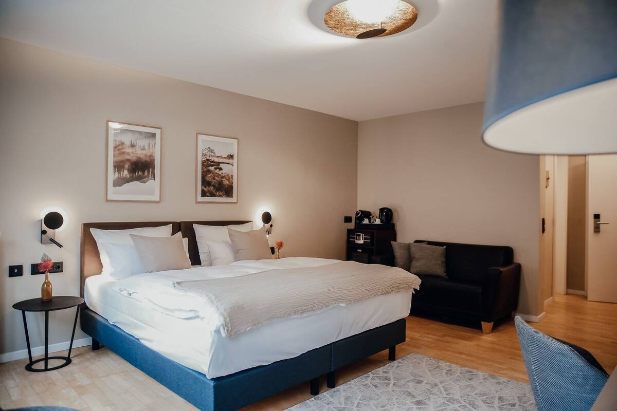 Camera da letto con un letto, comodini, una sedia, un divano e due quadri appesi alle pareti.
