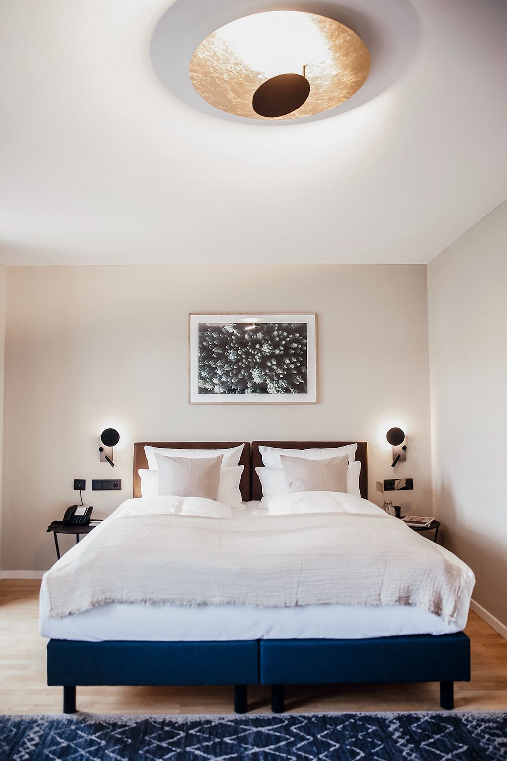 A modern bedroom with a large bed, two bedside tables, a wall-mounted artwork, and a unique circular ceiling light.
