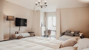 Een hotelkamer met een groot bed, een bureau met stoel, een aan de muur bevestigde televisie en een raam met gordijnen.