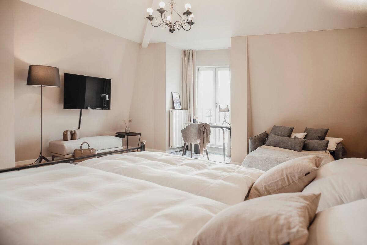 Camera d'albergo con un letto grande, una scrivania con sedia, una TV a parete e una finestra con tende.
