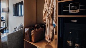 Een hotelkamer met zithoek, een badjas hangend op een rek, een minibar en een televisie.