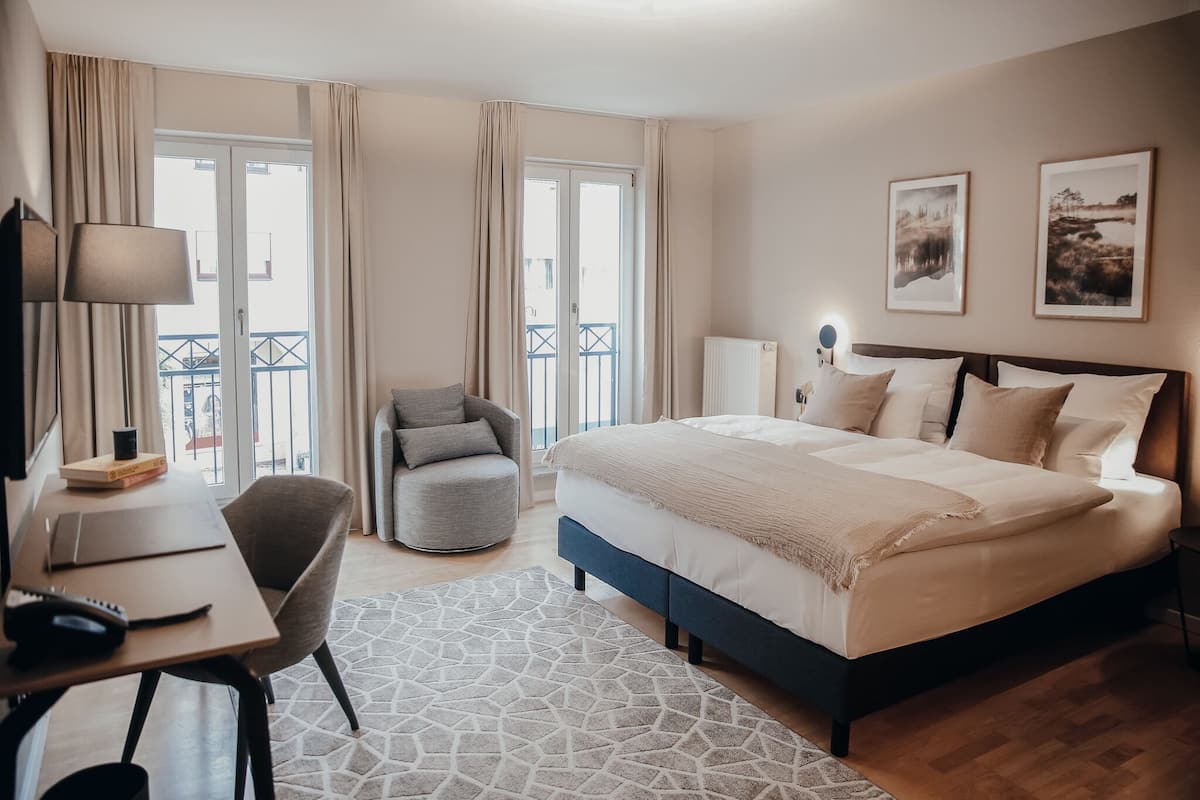 Una camera d'albergo con un letto, una scrivania con una lampada, una sedia e vista sul balcone esterno.