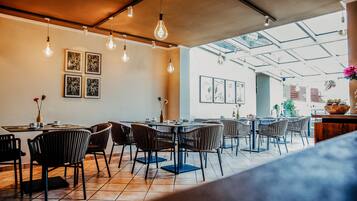 A restaurant with a modern interior, featuring exposed brick walls, hanging light fixtures, and a mix of wooden and metal furniture.