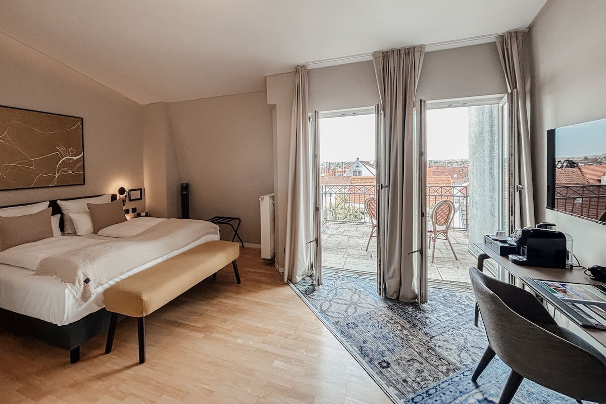 Una camera d'albergo moderna con un letto grande, una scrivania e un balcone con vista sulla città.