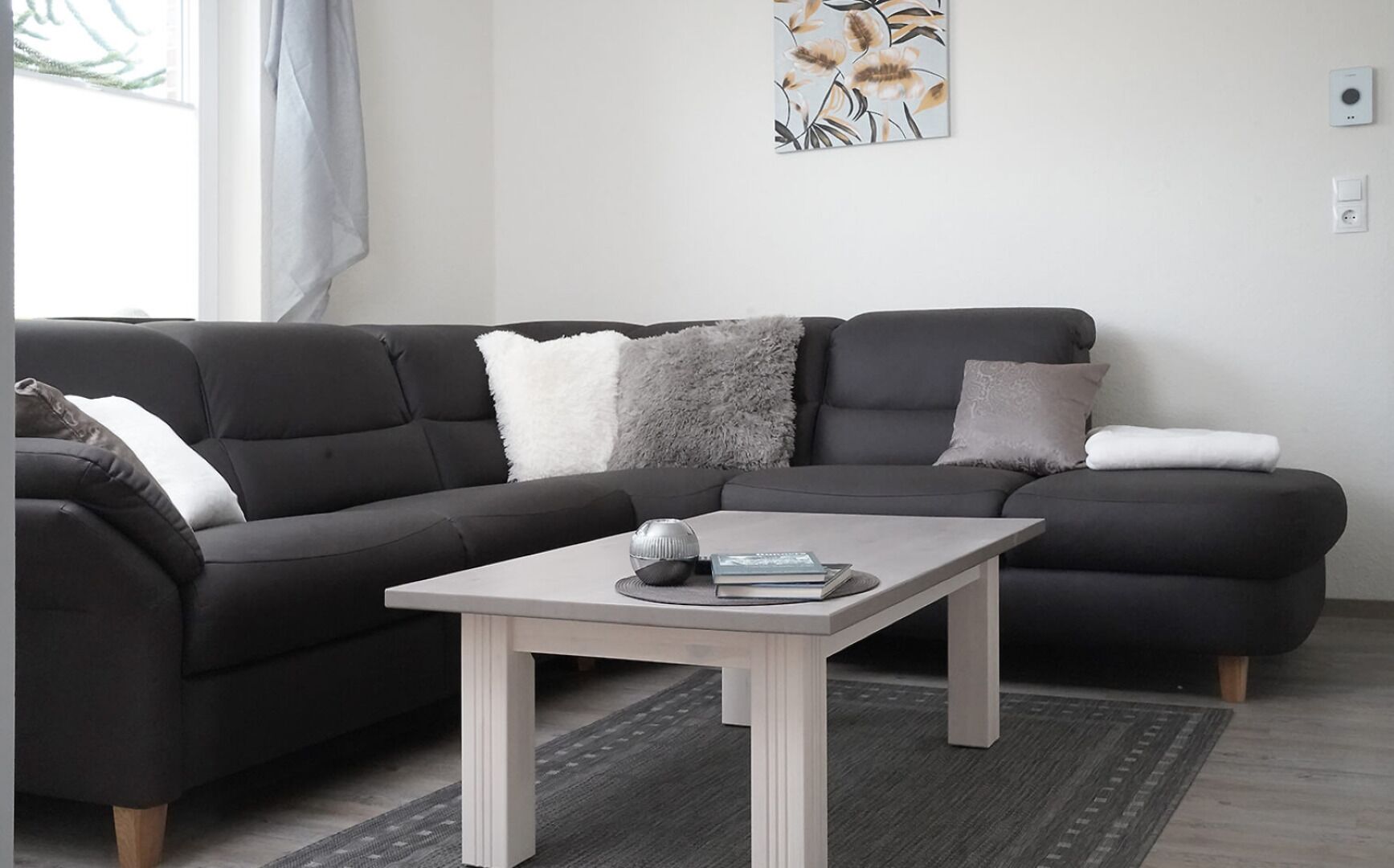 A modern living room with a dark grey sectional sofa, a light wooden coffee table, and a floral artwork on the wall.