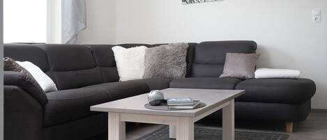 A modern living room with a dark grey sectional sofa, a light wooden coffee table, and a floral artwork on the wall.