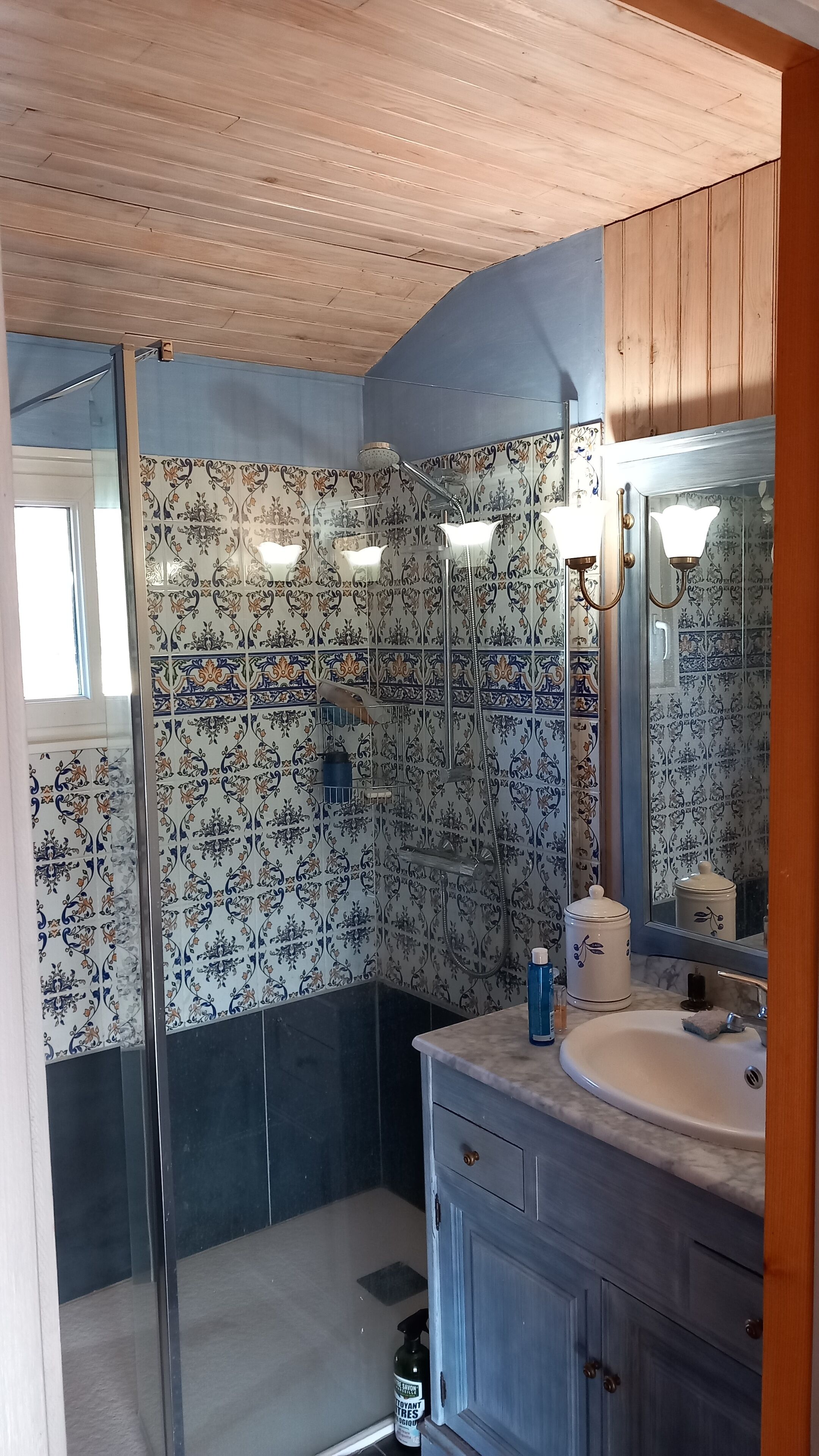 Een badkamer met patroon betegelde vloer, een douche, een wastafel en een spiegel.