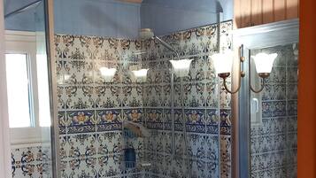 Een badkamer met patroon betegelde vloer, een douche, een wastafel en een spiegel.