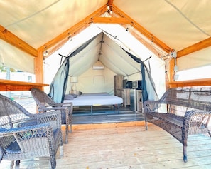 Acomodação em tenda com uma cama, uma pequena mesa com abajur e cadeiras de vime.