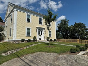A two-story house with a front porch, a small tree, and a wooden fence.