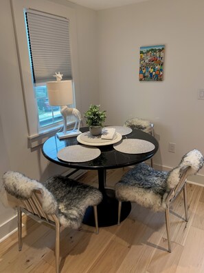 A dining area with a round table, four furry chairs, a potted plant, and a painting on the wall.