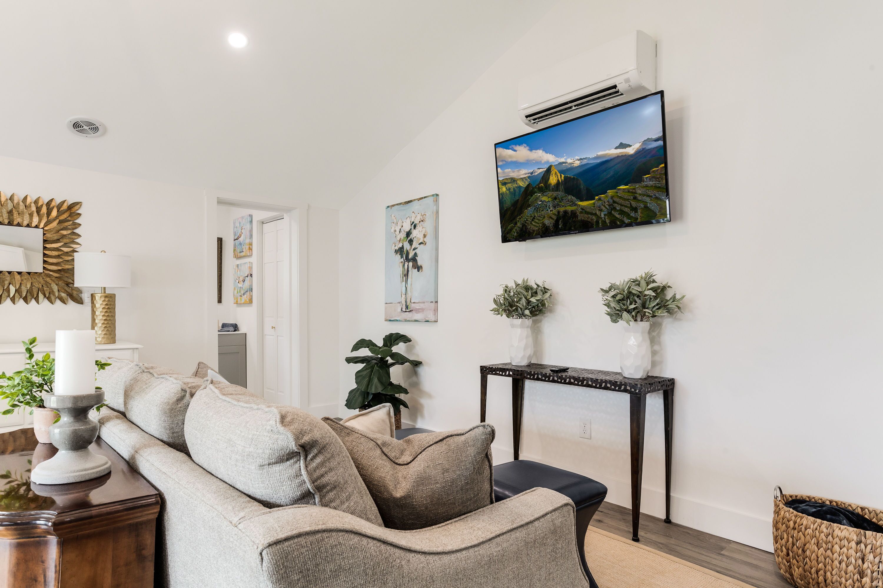 Un salon comprenant un canapé, une console ornée d’objets décoratifs, un téléviseur fixé au mur et une grande fenêtre.