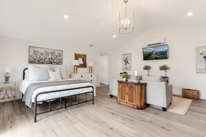 Un dormitorio con cama, mesitas de noche, cómoda, sofá y televisor.
