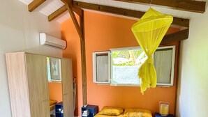 A bedroom with a bed, a wardrobe, a nightstand, and a window with a mosquito net. - Bunghello Village - Private Pool & Spa | Évasion Tropicale (Trois-Rivières)