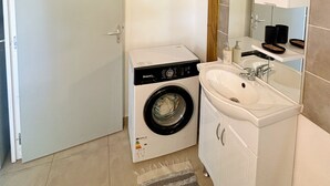 A compact laundry room with a washing machine, a sink, and a mirror. - Bunghello Village - Private Pool & Spa | Évasion Tropicale (Trois-Rivières)