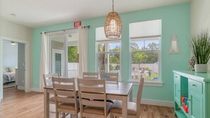 A dining area with a wooden table and chairs, a hanging light fixture, a window with a view of greenery, and a teal-colored cabinet with toys. - Pool & Hot Tub Home (St. Augustine)