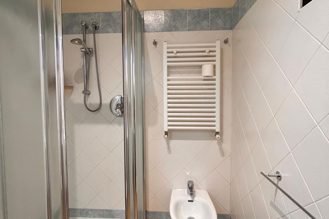 Un bagno con doccia vetrata, un lavandino a colonna bianco e un portascopevoli.
